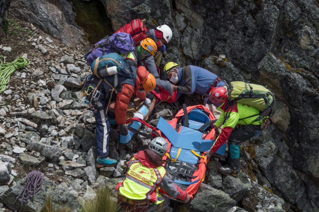 Rescue team assisting injured hiker on rocky mountainside with stretcher.